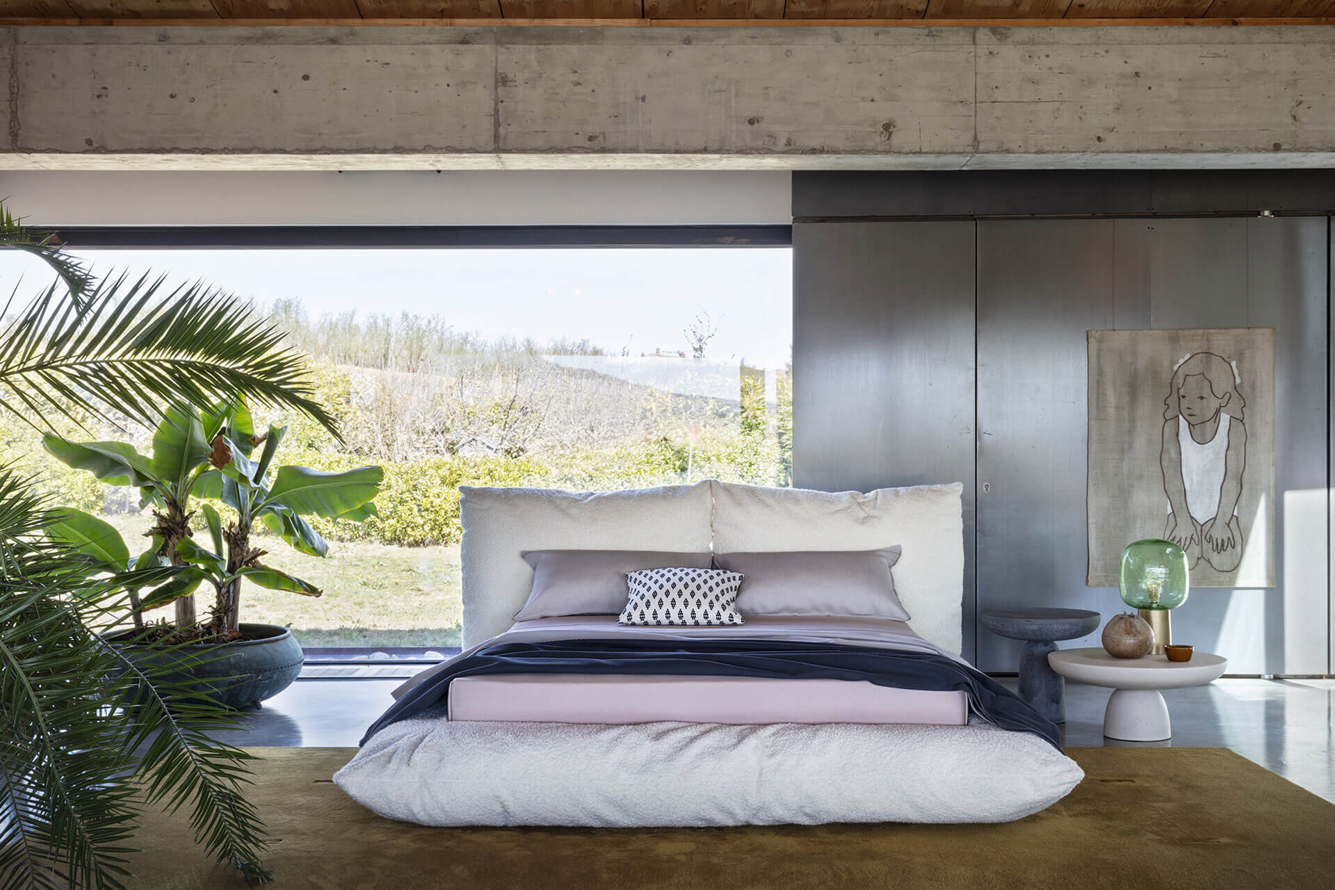 Modern minimalist bedroom with a low bed frame, neutral bedding, and large windows overlooking greenery