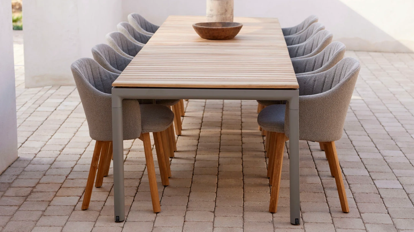 Modern outdoor dining table with wooden top and grey cushioned chairs on a tiled patio