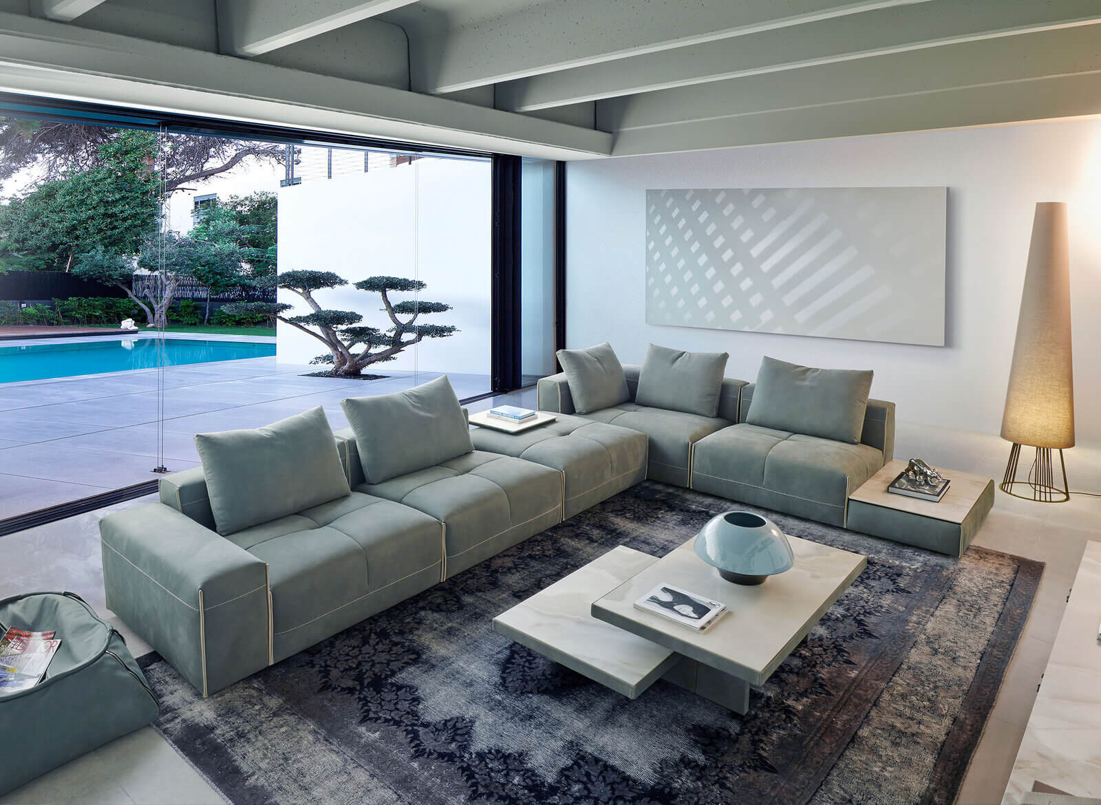 Contemporary living room with a large sectional sofa, modern coffee table, floor lamp, and poolside view through sliding glass doors.