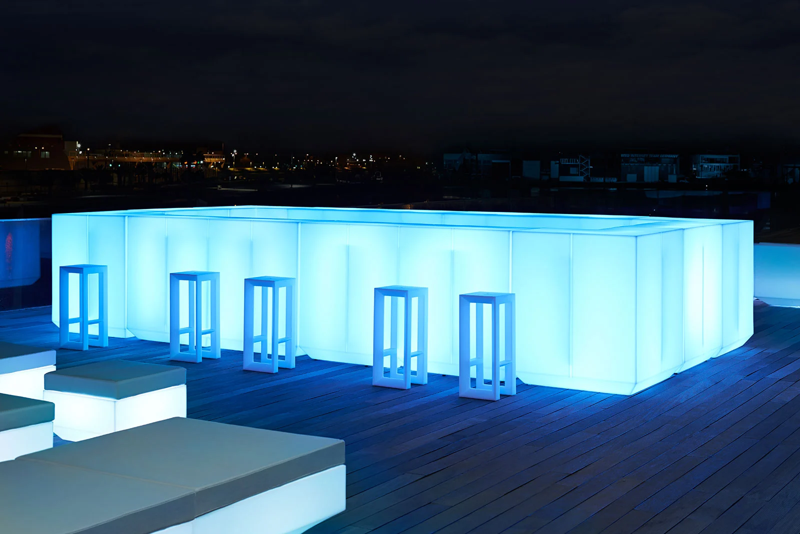 Luxury counter stools with a minimalist white frame design at a glowing blue illuminated outdoor bar.